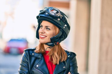 Şehirde motosiklet kaskı takıp gülümseyen genç Latin kadın..