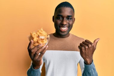 Genç Afro-Amerikan adam, elinde fırınlanmamış spagettiyle başparmağını yana kaldırmış, ağzı açık gülümsüyor. 