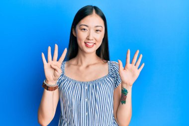 Gündelik çizgili tişört giyen genç Çinli kadın dokuz numaralı parmaklarıyla gösteriş yapıyor ve gülümsüyor. Kendinden emin ve mutlu.. 