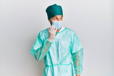 Cerrah üniforması ve tıbbi maske takan genç yakışıklı adam gergin ve elleri ağız yiyen tırnaklarla gergin görünüyor. anksiyete. 