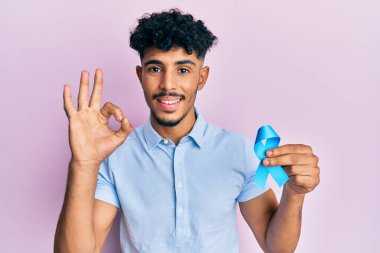 Genç Arap yakışıklı adam mavi kurdele tutuyor. Parmaklarıyla imza atıyor. Gülümsüyor. 