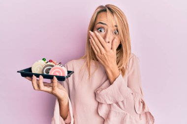 Güzel sarışın kadın elinde pasta şekerlemeleri ile ağzını eliyle kapatıyor, şaşırmış ve hata yapmaktan korkuyor. şaşırmış ifade 