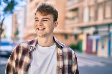 Genç beyaz adam gülümseyerek şehirde mutlu mesut duruyor..