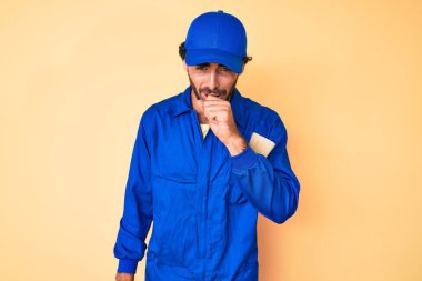 Kıvırcık saçlı, ayı kılıklı, işçi tulumu giyen, kendini iyi hissetmeyen ve soğuk algınlığı veya bronşitin belirtisi olarak öksüren yakışıklı bir genç. sağlık hizmeti kavramı. 