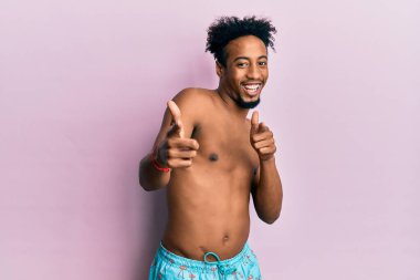 Sakallı, mayo giymiş, mutlu ve komik yüzüyle kamerayı işaret eden Afro-Amerikan bir genç. iyi enerji ve titreşimler. 