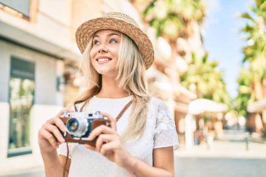 Beyaz tenli genç turist kız şehrin caddesinde klasik kamera kullanarak mutlu bir şekilde gülümsüyor..