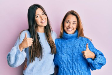 Kışlık yün süveter giyen İspanyol anne ve kız aileleri mutlu bir el hareketi yapıyorlar. Kameraya bakıp başarıyı gösteren ifade. 
