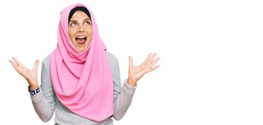 Geleneksel İslami başörtüsü takan genç beyaz kadın deli gibi bağırıyor ve agresif bir ifadeyle bağırıyor ve kollarını kaldırıyor. hüsran kavramı. 