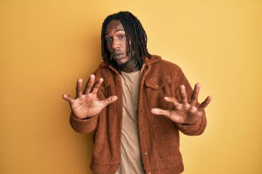 Kahverengi retro ceket giyen Afrika kökenli Amerikalı adam korku ifadesinden korkuyor ve dehşete düşüyor. El hareketlerini durdur, şok içinde bağır. panik konsepti. 