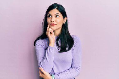 Elleri çenesinde gündelik kıyafetler giyen genç İspanyol kadın soru sormayı düşünüyor, düşünceli bir ifade. Gülümseyen ve düşünceli bir yüz. şüphe kavramı. 