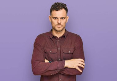 Gündelik kıyafetler giyen, kuşkucu ve gergin genç İspanyol bir adam. Yüzünde çapraz kollarla onaylamayan bir ifade var. negatif kişi. 