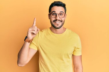 Gündelik kıyafetler giyen ve gözlüklü genç İspanyol başarılı bir fikirle işaret ediyor. Heyecanlı ve mutlu. Bir numara.. 