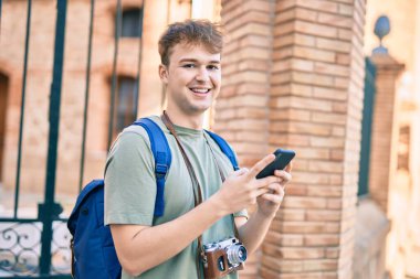 Kafkasyalı genç turist şehirde akıllı telefon kullanarak mutlu bir şekilde gülümsüyor.