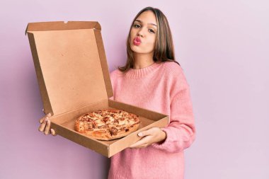 Genç esmer kadın elinde İtalyan pizzasıyla kameraya bakıp öpüşürken çok güzel ve seksi görünüyor. aşk ifadesi. 