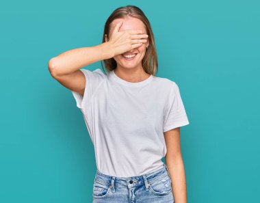 Gayri resmi beyaz tişört giyen güzel sarışın kadın. Gülümsüyor ve elleri yüzünde, şaşırtmak için gözleri kapatıyordu. kör kavram. 