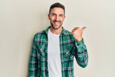 Sakallı, sıradan giyinen, mutlu yüzlü, gülümseyen ve baş parmağıyla yüzünü gösteren yakışıklı bir adam.. 