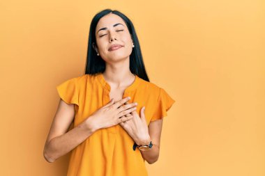 Güzel, genç bir kadın gündelik giysiler giyip, elleri göğsünde, gözleri kapalı ve yüzünde minnet dolu bir jest yapıyor. sağlık kavramı. 