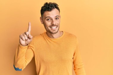 Bir fikir veya soruyla gülümseyen gündelik kıyafetler giyen genç İspanyol adam, bir numara, mutlu bir yüzle işaret ediyor. 