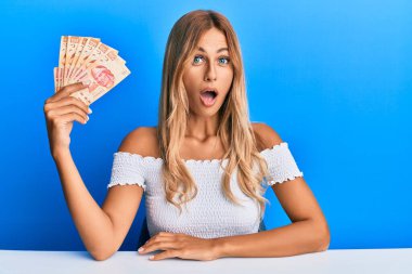Güzel sarışın kadın elinde 100 Meksika pezosu tutuyor. Korkmuş ve şaşkın bir şekilde ağzı açık kalmış, inançsız bir yüz. 