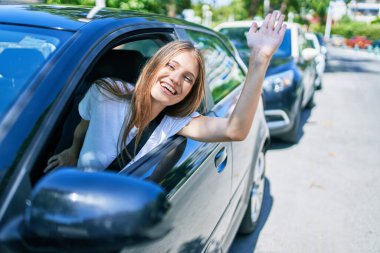 Genç, güzel, sarışın, gülümseyen bir kadın, mutlu bir şekilde arabada oturuyor ve gülümsüyor.