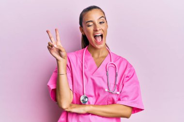 Genç İspanyol kadın doktor üniforması giyiyor ve steteskop gülüyor kameraya göz kırparak zafer işareti yapıyor. İki numara.. 