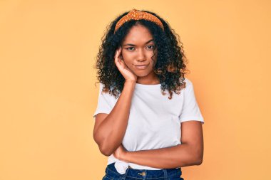 Genç Afro-Amerikalı kadın günlük kıyafetler giyip kollarını kavuşturarak depresyondan sıkılmış ve yorgun görünüyor.. 