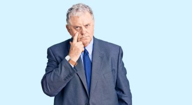 İş ceketi giymiş yaşlı, gri saçlı bir adam senin jestini seyrediyor, şüpheli bir ifade. 