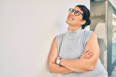 Genç ve cüsseli bir kadın gülümsüyor. Şehrin duvarına yaslanmaktan mutlu..