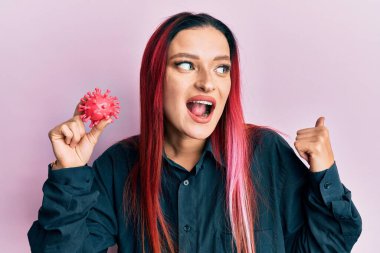 Elinde virüs oyuncağı olan beyaz bir kadın başparmağını kaldırıyor ve ağzı açık gülümsüyor. 