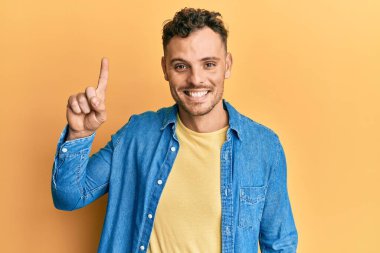 Bir fikir veya soruyla gülümseyen gündelik kıyafetler giyen genç İspanyol adam, bir numara, mutlu bir yüzle işaret ediyor. 