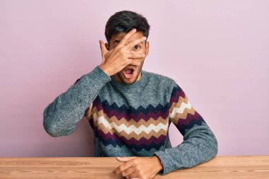 Kış süveteri giymiş genç yakışıklı bir adam masanın üzerinde oturuyor. Şok olmuş bir şekilde yüzünü ve gözlerini eliyle kapatıyor, parmaklarından korkuyla bakıyor. 