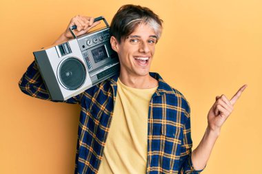 Latin kökenli genç adam müzik kutusunu tutuyor, gülümsüyor mutlu bir şekilde elleri ve parmakları kenarda işaret ediyor. 