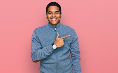 Genç, yakışıklı İspanyol bir adam, günlük kazak giyiyor. Neşeli, yüzünde bir gülümseme var. Yüzünde mutlu ve doğal bir ifade var. 