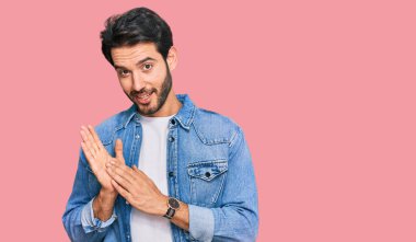 Latin asıllı genç adam, günlük kıyafetler giyip alkışlıyor ve mutlu, neşeli ve gururlu elleri bir arada alkışlıyor. 