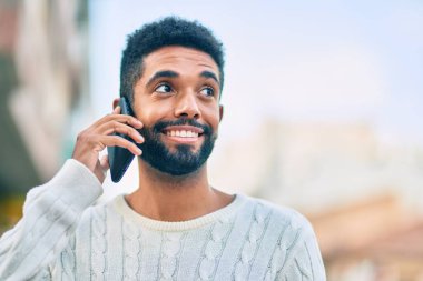 Genç Afrikalı Amerikalı gülümseyen mutlu bir adam şehirdeki akıllı telefondan konuşuyor..