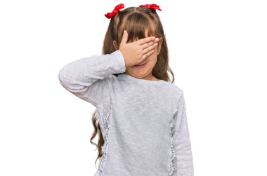 Sıradan kıyafetler giyen, gülümseyen ve elleri yüzünde, şaşırmak için gözlerini kapatan beyaz bir kız çocuğu. kör kavram. 