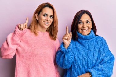 Latin anne ve kızı gündelik kıyafetler giyip bir fikir veya soruyla gülümsüyor ve mutlu bir yüzle işaret ediyor. 