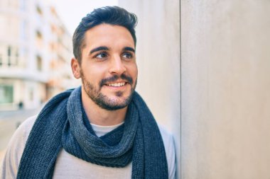 Genç İspanyol adam mutlu bir şekilde gülümsüyor. Şehrin duvarına yaslanmış bir eşarp takıyor.