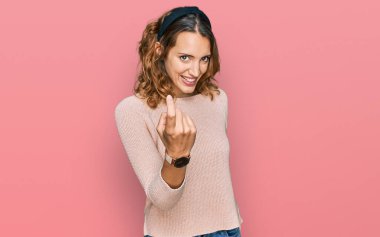 Güzel, beyaz bir kadın, sıradan bir süveter giyiyor. Buraya el hareketleriyle, mutlu bir şekilde karşılamaya ve gülümsemeye davet ediyor. 