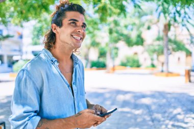 Şehrin caddesinde akıllı telefon kullanan, mutlu gülümseyen genç İspanyol adam.