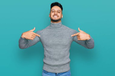 Gündelik giysiler giyen genç bir Arap. Kendine güvenen, gülümseyen, kendini gururlu ve mutlu gösteren bir adam.. 