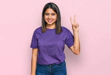 Gündelik mor tişört giyen genç İspanyol kız iki numarayı gösterip işaret ederken kendinden emin ve mutlu gülümsüyor.. 