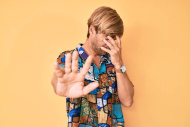 Yazlık tişört giyen, gözlerini elleriyle kapatan ve üzgün ve korku ifadeleriyle jest yapan genç sarışın adam. utangaç ve olumsuz kavram. 