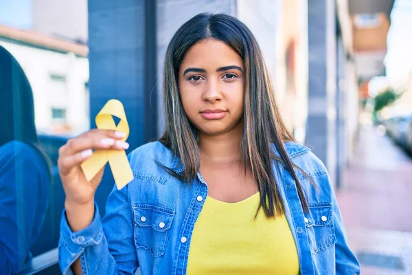 Young latin woman with serious expression holding yellow ribbon at city.