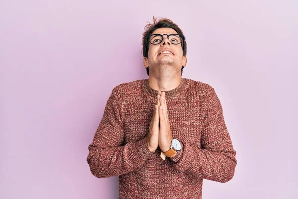 Handsome caucasian man wearing casual sweater and glasses begging and praying with hands together with hope expression on face very emotional and worried. begging.