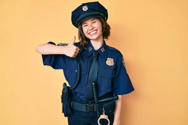 Young beautiful woman wearing police uniform doing happy thumbs up gesture with hand. approving expression looking at the camera showing success.