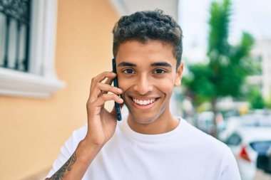 Genç Latin adam gülümsüyor ve şehirde akıllı telefondan konuşuyor..