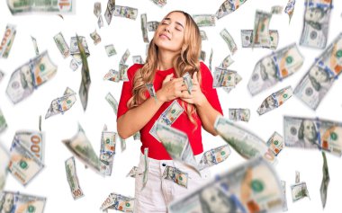 Genç, güzel, sarışın bir kadın sıradan kıyafetler giyiyor. Elleri göğsünde, gözleri kapalı gülümsüyor ve yüzünde minnet ifadesi var. sağlık kavramı.