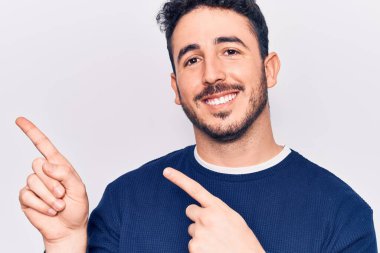 Gündelik kıyafetler giyen genç İspanyol adam gülümseyip kameraya bakıyor ve iki eliyle ve parmaklarıyla kenarı işaret ediyor.. 