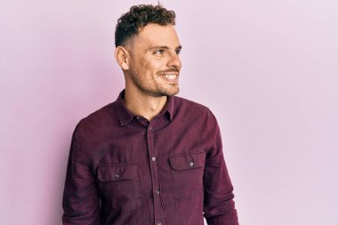 Latin kökenli genç bir adam günlük giysiler giyiyor, rahat bir görünüm takınıyor, doğal bir yüz ifadesi ve kendinden emin bir gülümsemeyle poz veriyor.. 